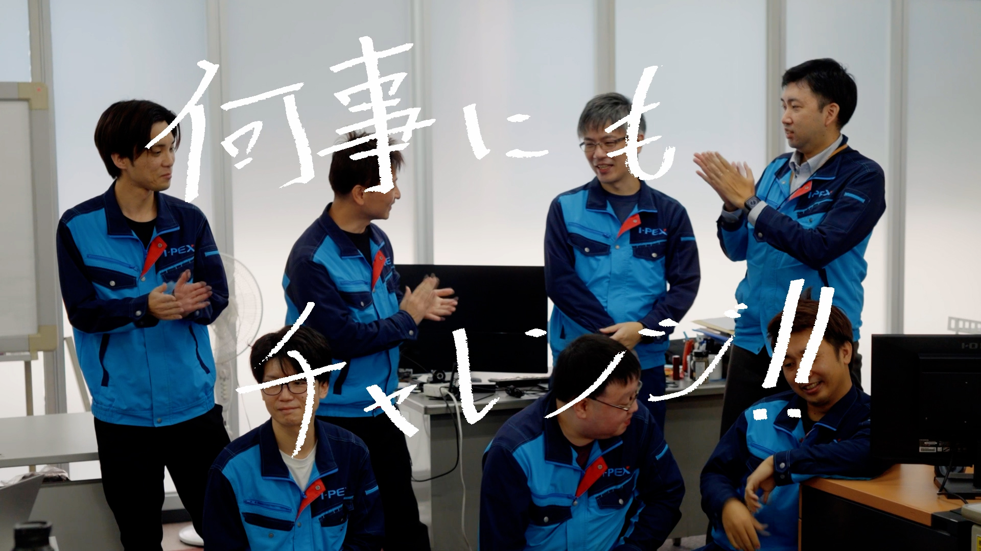 生産企画のNさんの書いた「何事にもチャレンジ！！」の文字と、部署の皆さんがNさんに拍手している様子
