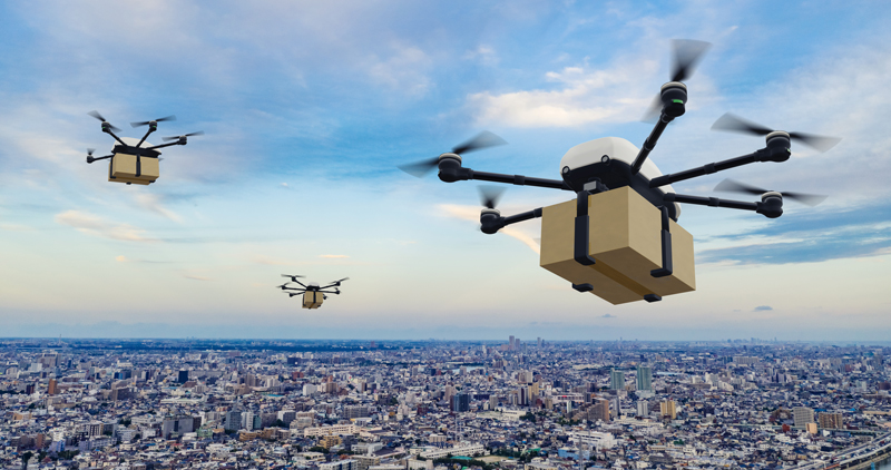 複数のドローンが荷物を搭載し都市上空を飛行するイメージ